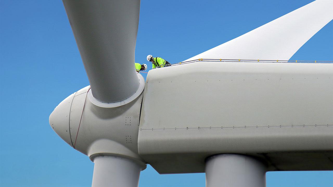 Workers in personal protective equipment work on the nacel of a wind turbine