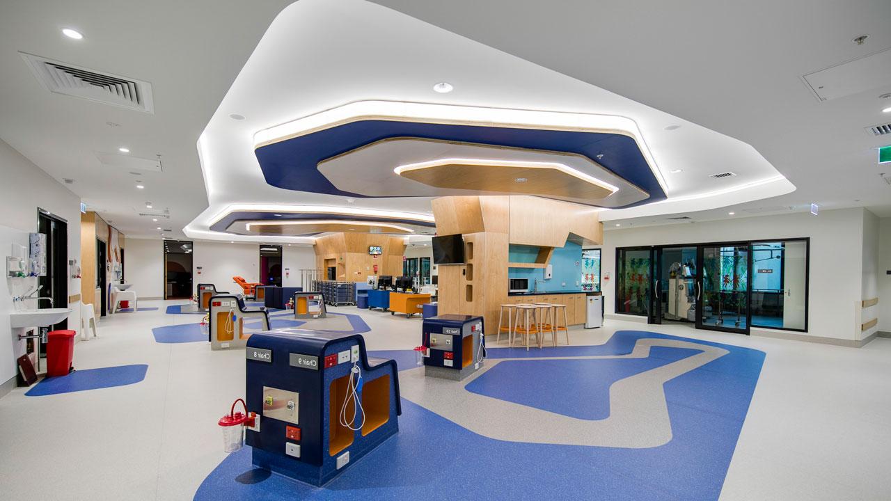 A hospital treatment area with blue and white geometric designs on the floor that are echoed in the ceiling and lighting treatment