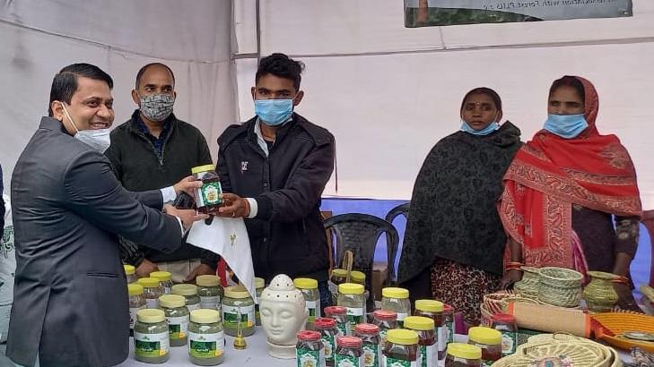 A group of people standing next to a table with jars as part of a Moringa leaf value chain set up by Tetra Tech’s Forest-PLUS 2.0